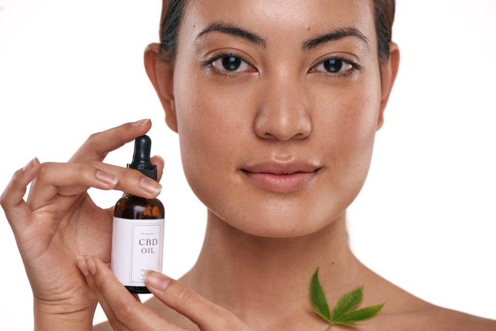 Shot of a beautiful young woman holding a bottle of CBD oil against a white background